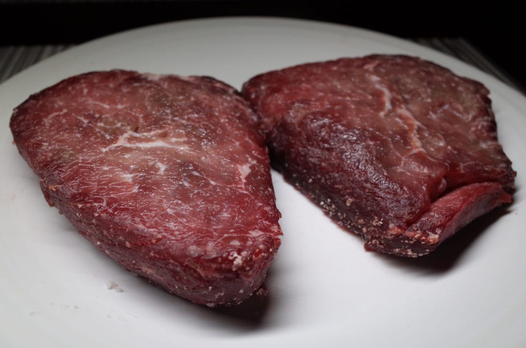 Two rinsed sirloin steaks on a white plate.