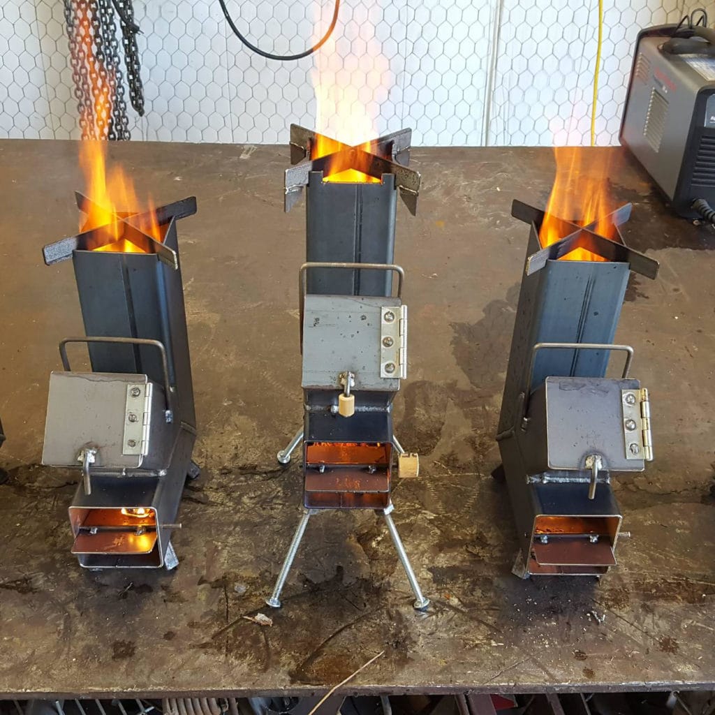 Three handmade rocket stoves lit on a workshop floor