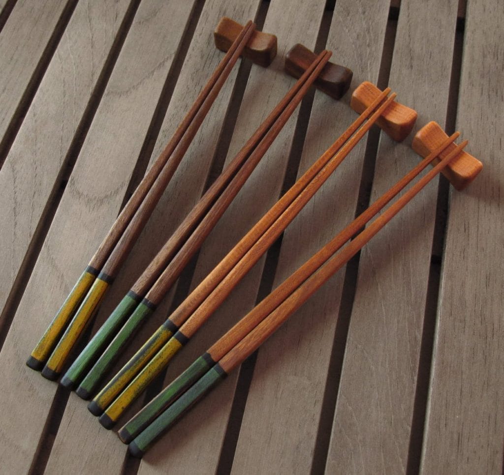 Four sets of handmade and hand painted chopsticks set against a wooden background