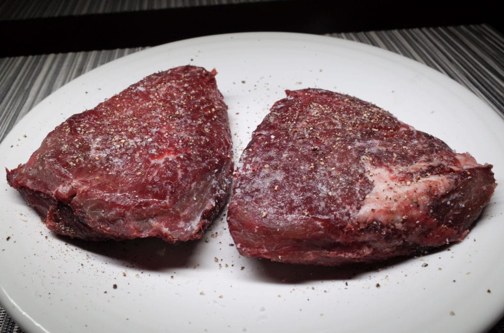Two seasoned sirloin steaks after Koji Powder preparation on a white plate ready for the grill.
