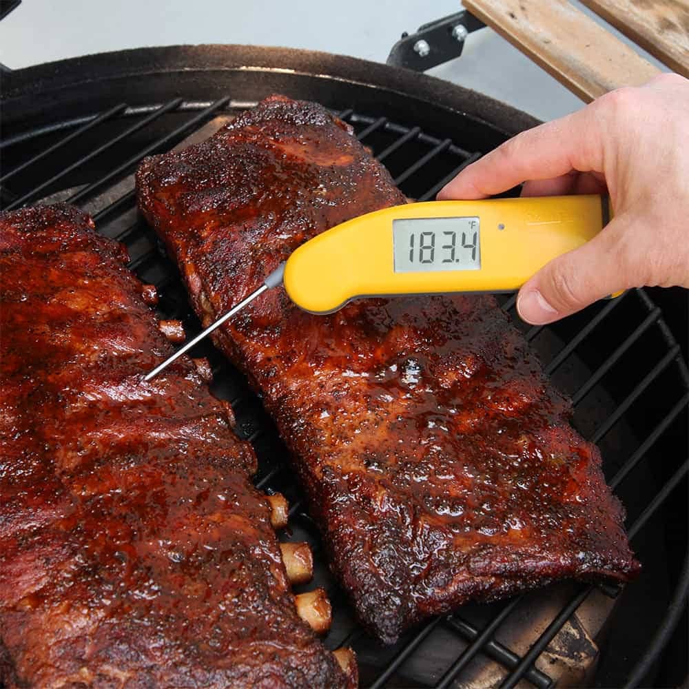 A yellow ThermoWorks Thermapen probe thermometer being used to check the temperature of grilled ribs.