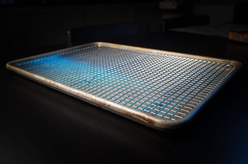 A Volrath sheet pan and Culinary Institute of America Cooling Rack on a black table.