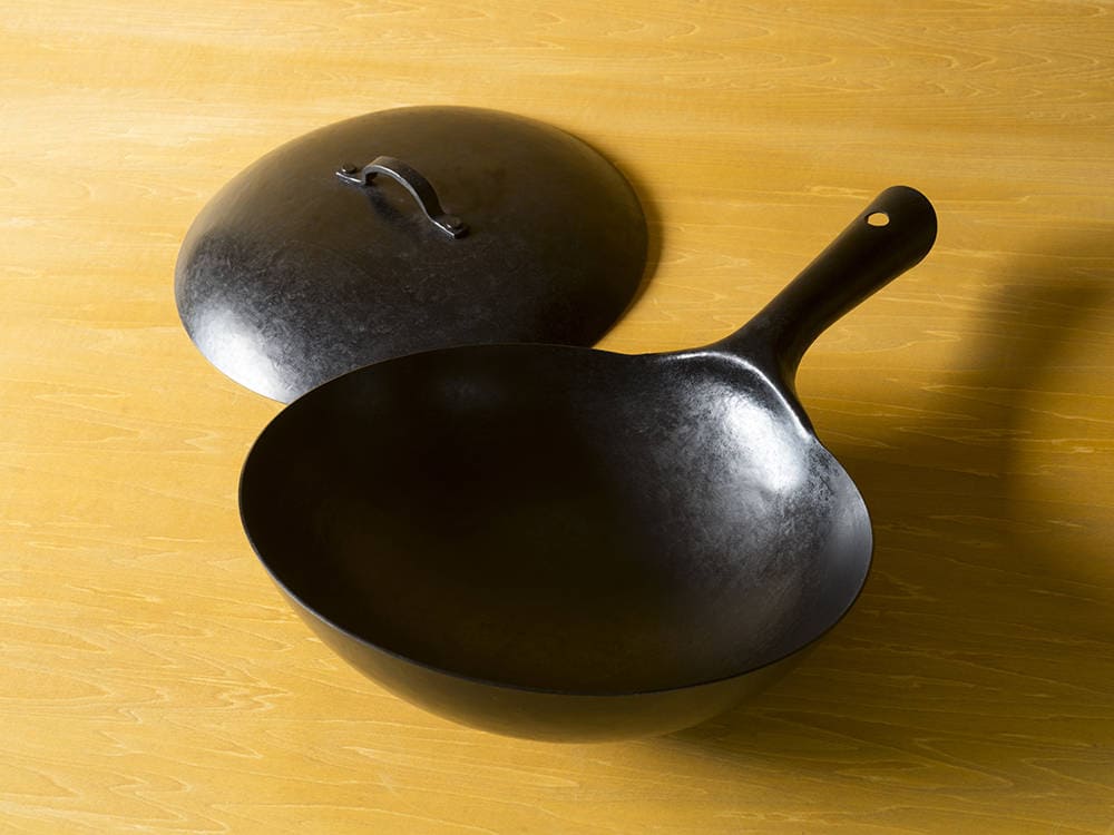 A hand hammered iron wok on a wood background