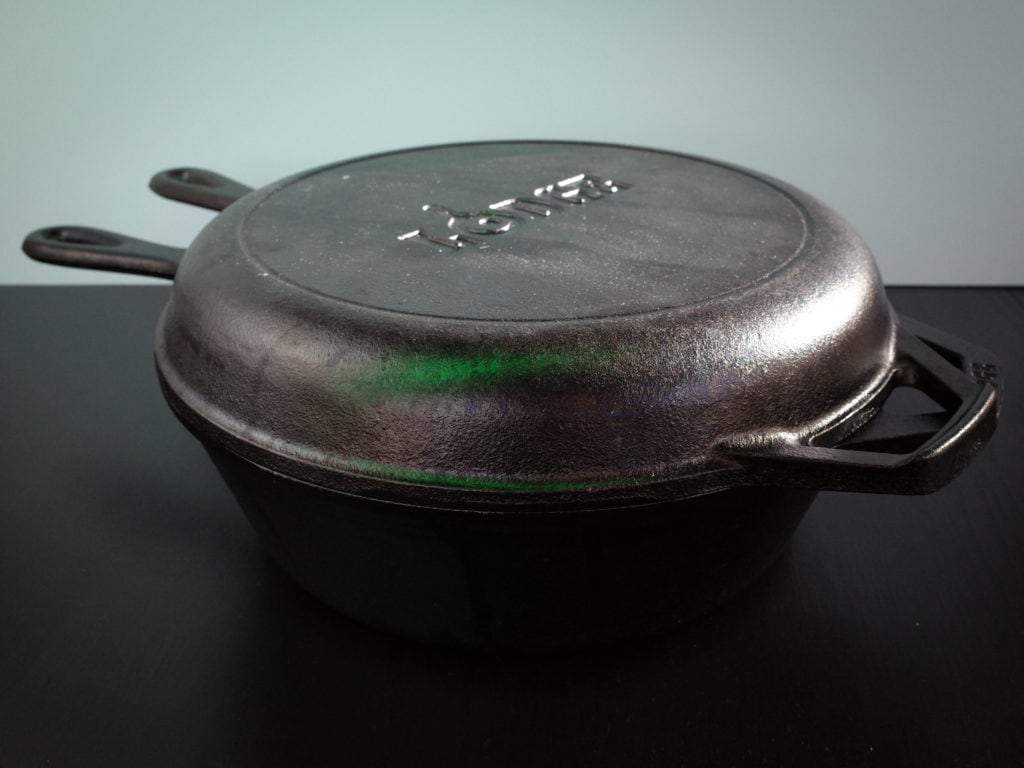 A Lodge 3.2 quart cast iron combo cooker which includes both a deep skillet and a shallow frying pan on a black table.