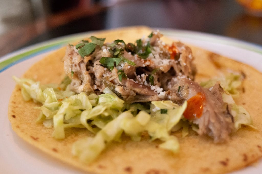 A duck confit taco on a white paper plate.